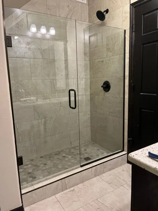 Modern bathroom with glass-enclosed tiled shower, black fixtures, and beige floor tiles