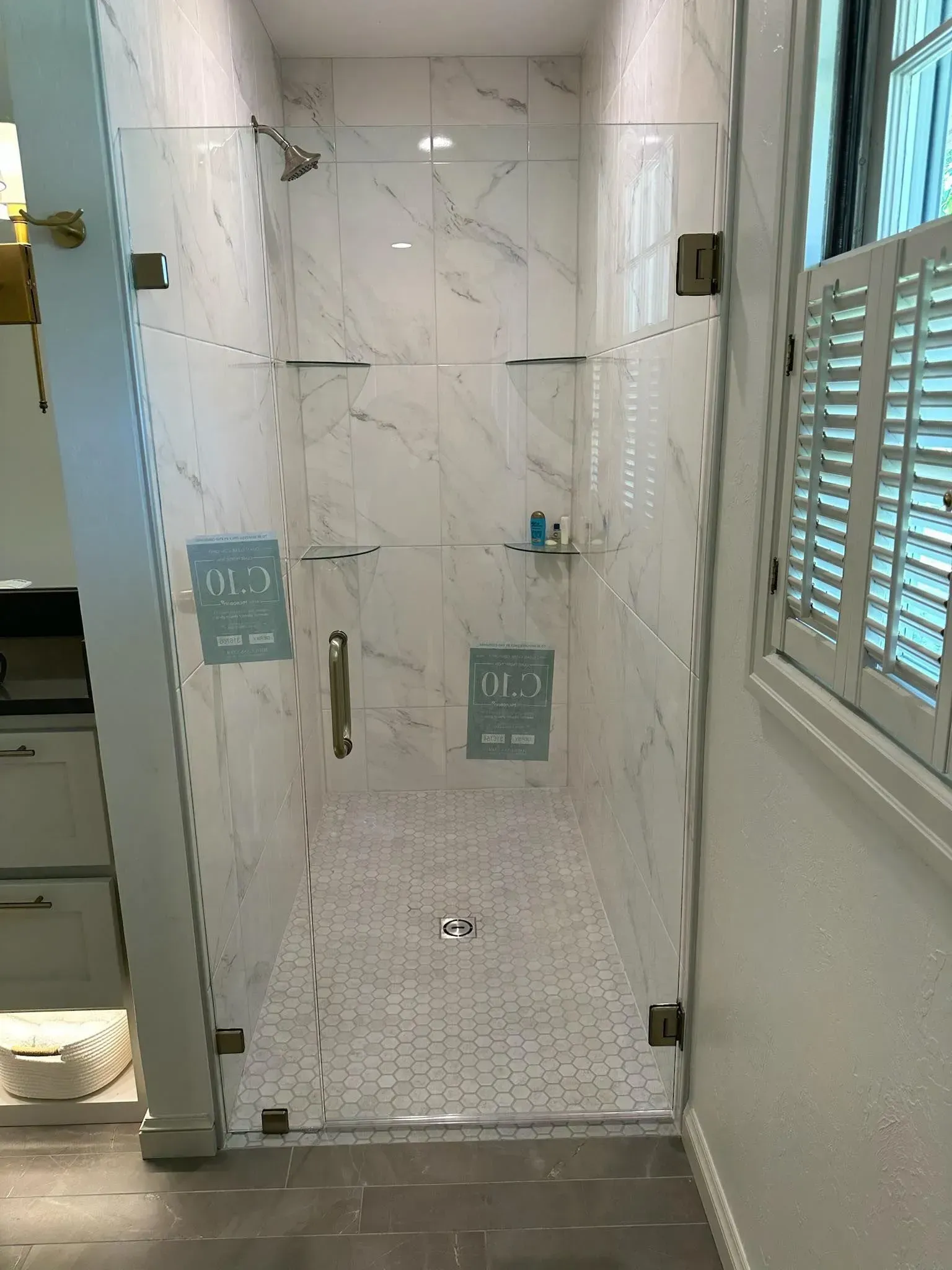 Walk-in shower with white marble-look tile, glass door, grab bars, and a built-in bench in a bathroom