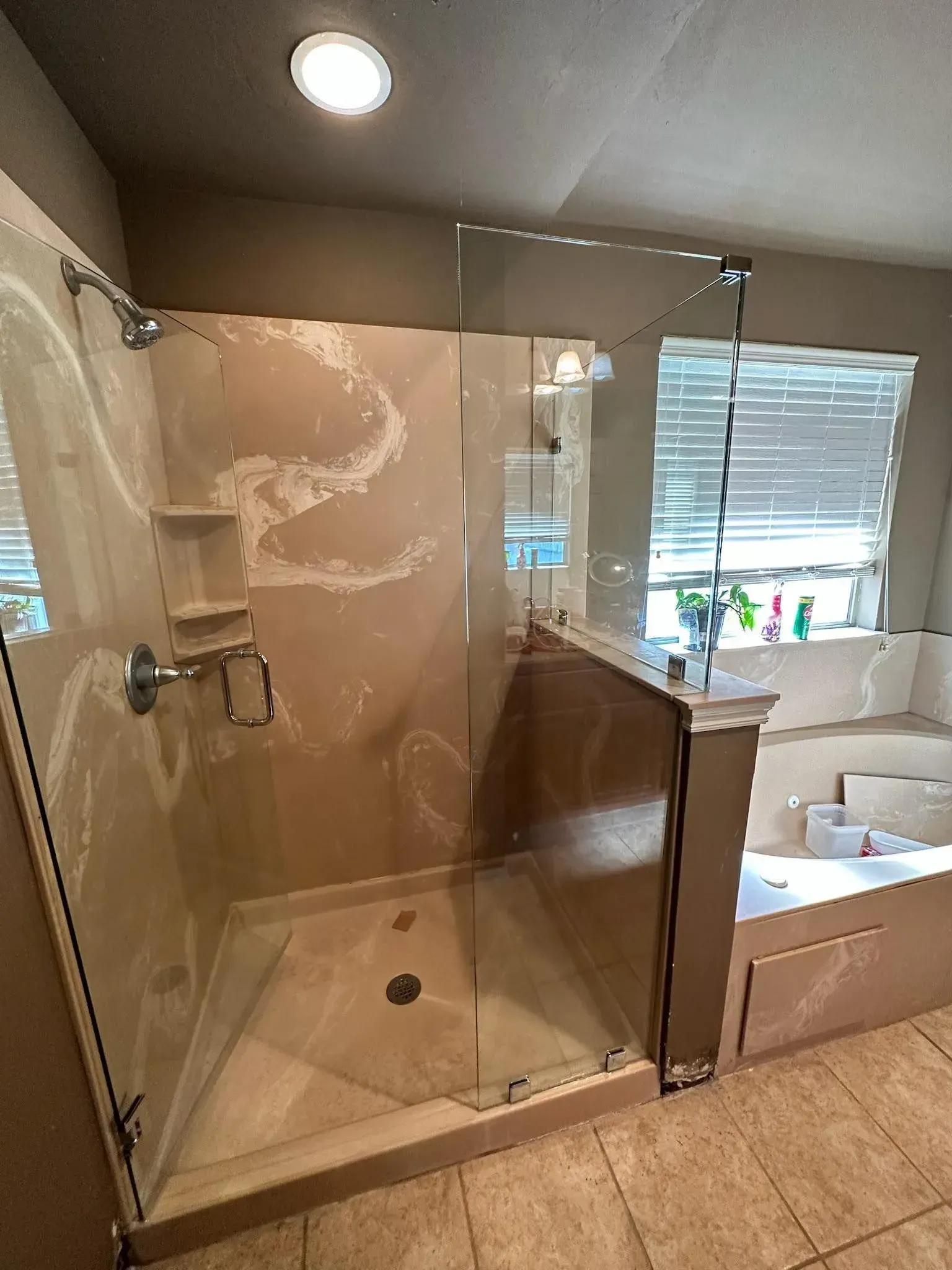 Glass shower stall with beige tile, wooden vanity, and bright window above a bathtub sink area