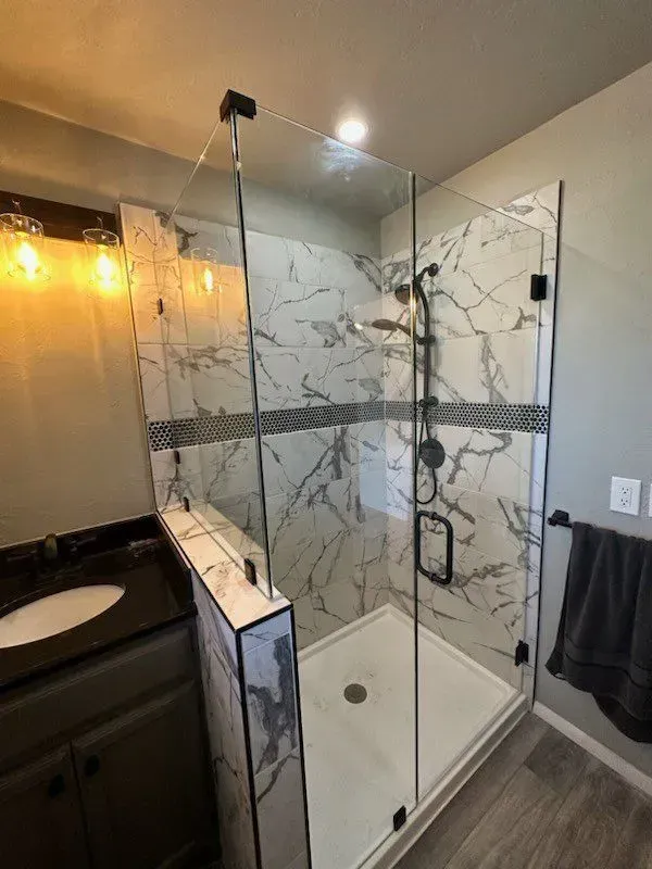 Glass walk-in shower with marble-look tile, black fixtures, and a dark vanity in a modern bathroom