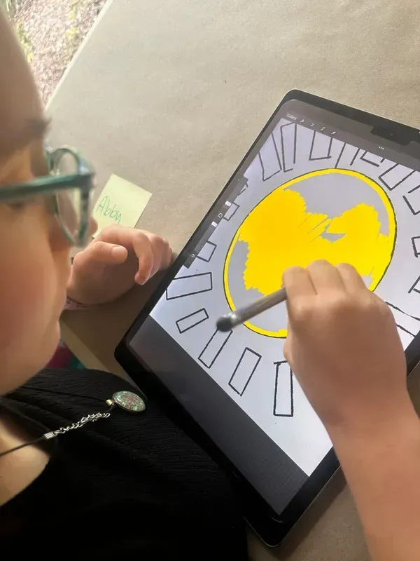 Person drawing on a tablet with a stylus. The drawing is of a yellow sun with gray rays.