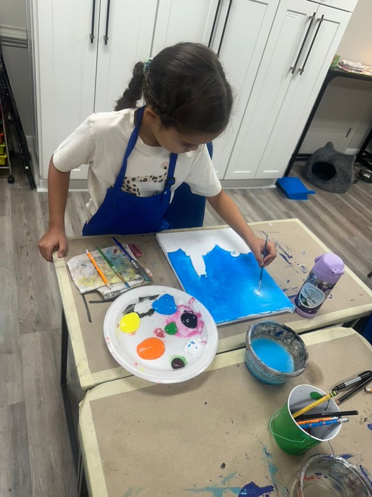 A child paints on a canvas, surrounded by paint supplies on a table.