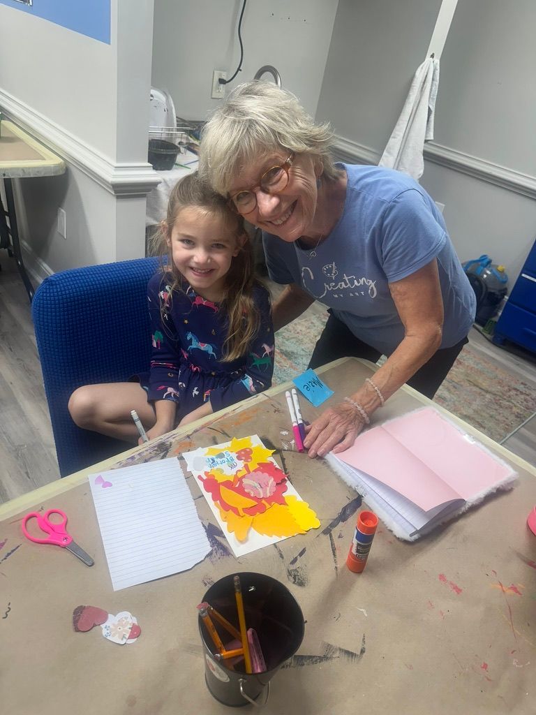 Woman and girl smiling together at art table with supplies.