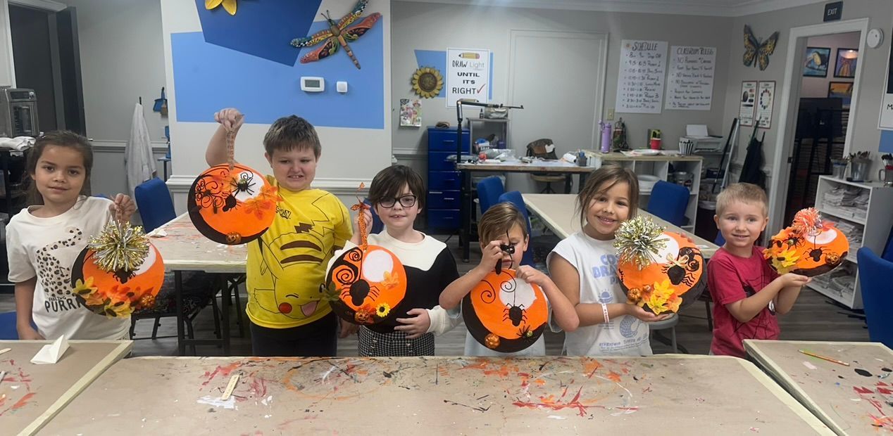 Children in a classroom show off their Halloween crafts: orange and black lanterns.