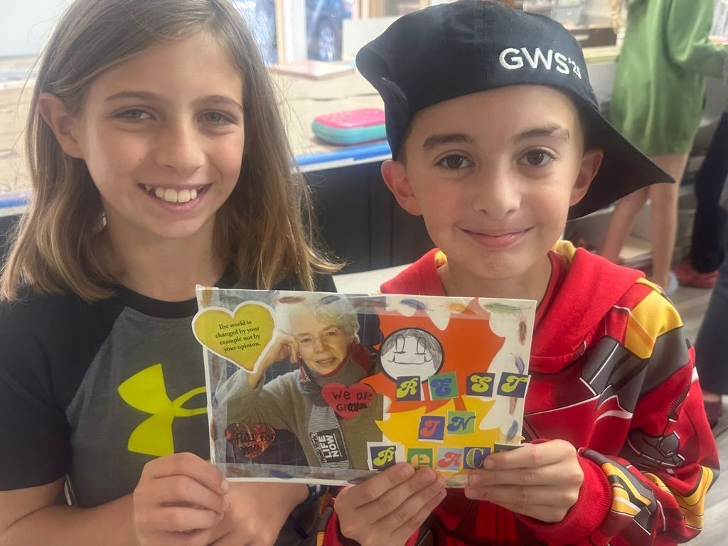 Two children holding a handmade card with a photo. Boy wears a hat, girl smiles.