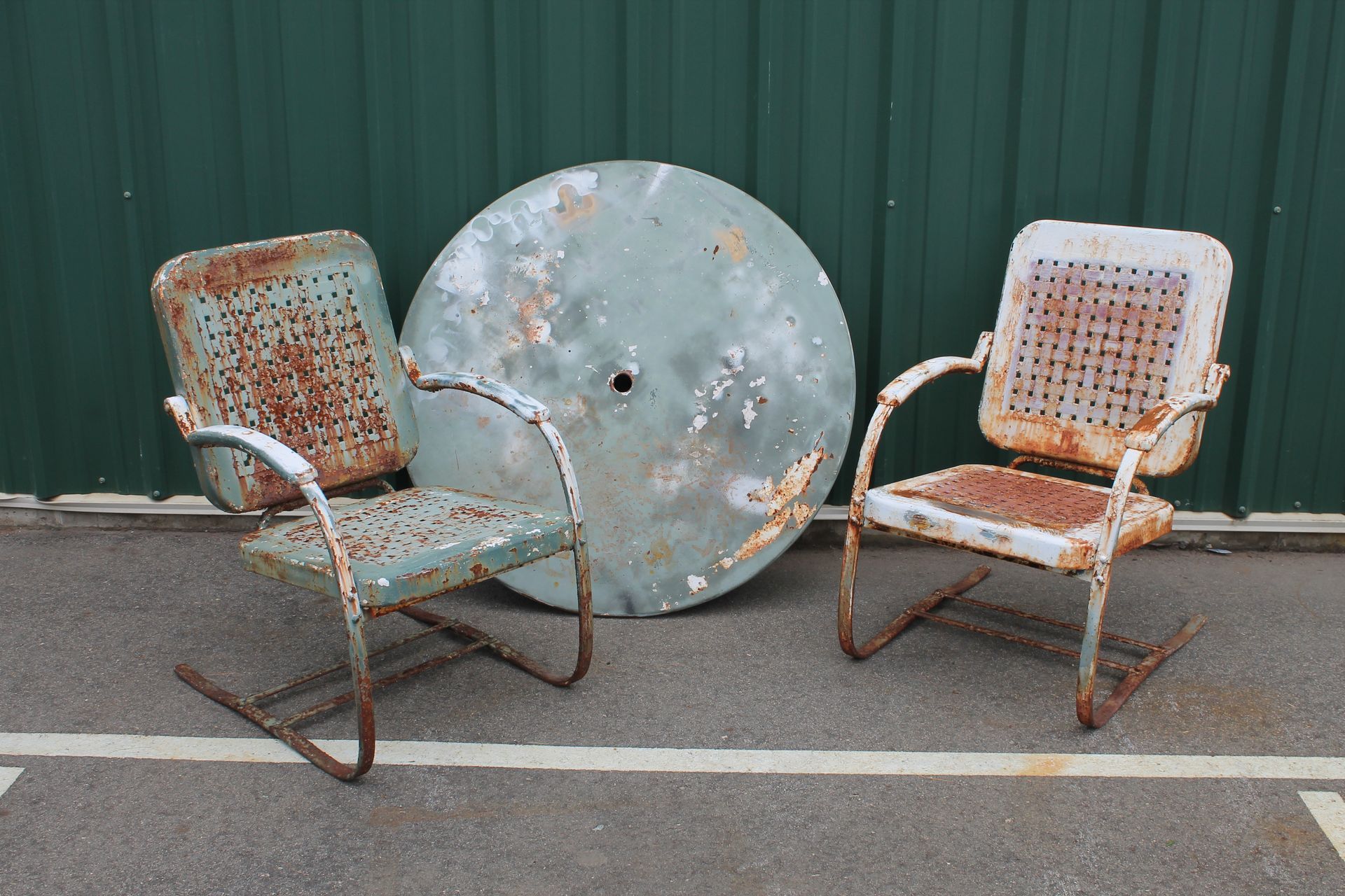 Two rusty chairs are sitting next to a green umbrella.