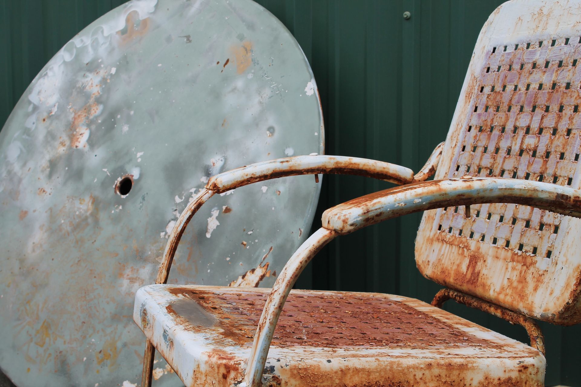 A rusty chair is sitting next to a green table.