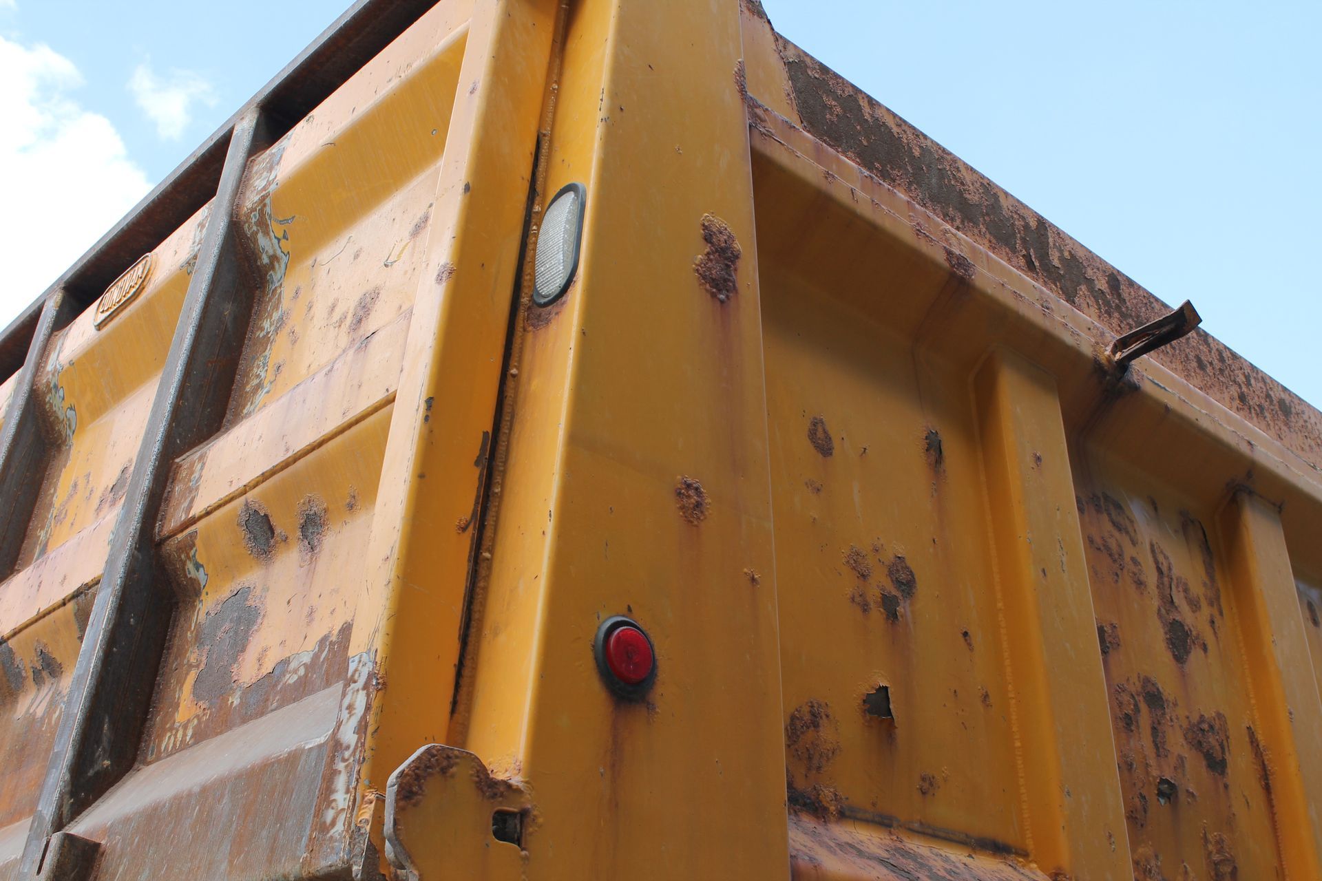 The back of a yellow dump truck with a red light on it.