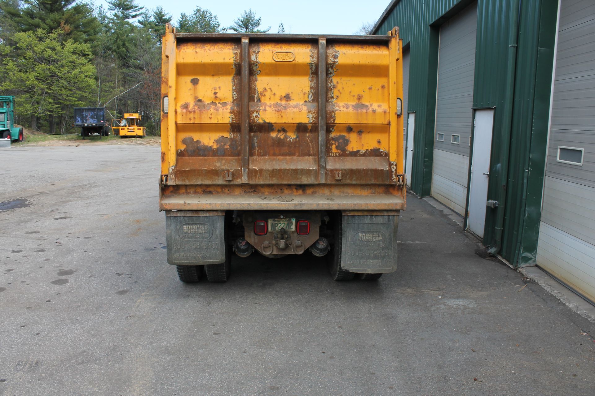 A yellow dump truck is parked in front of a green building