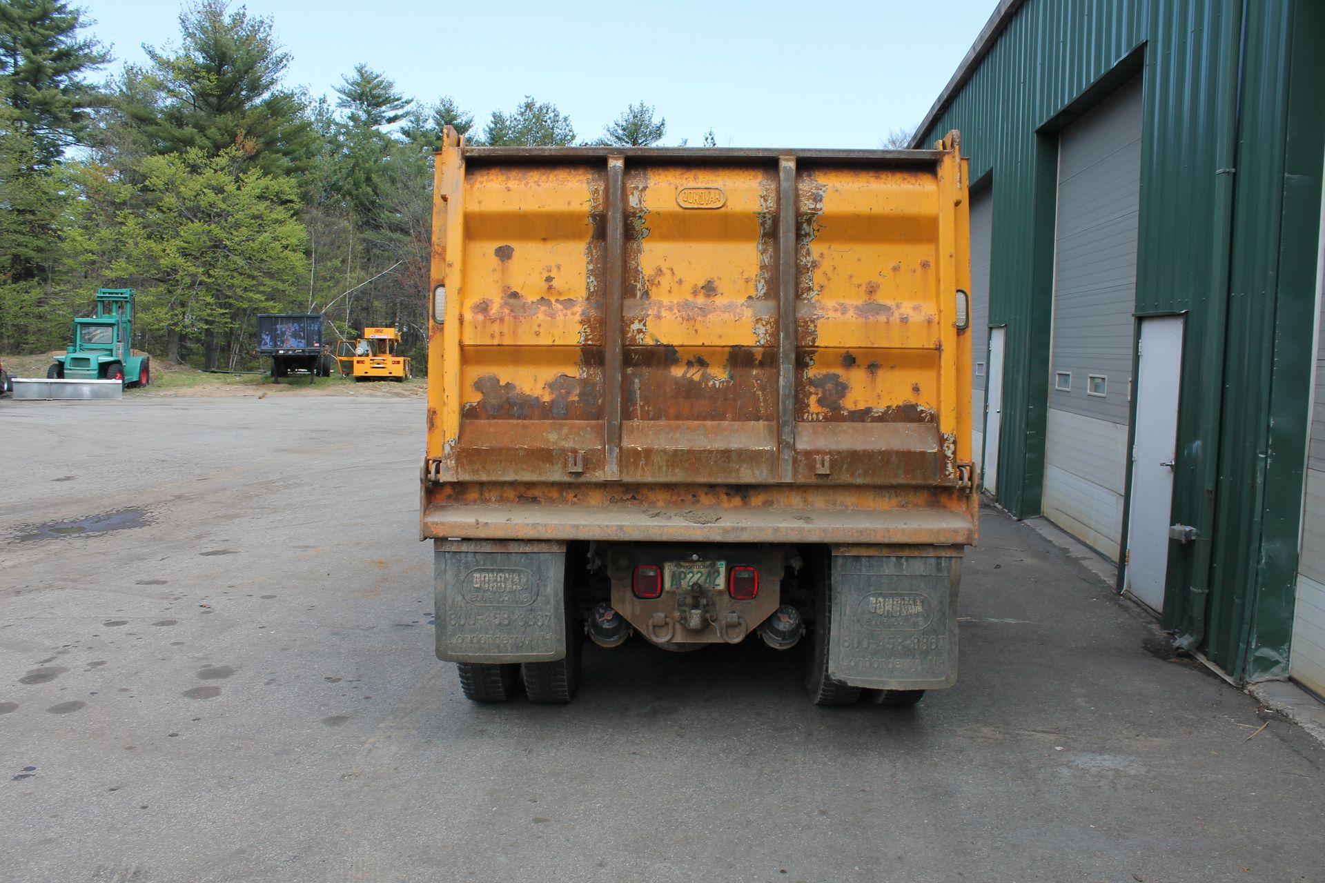 A yellow dump truck is parked in front of a green building.