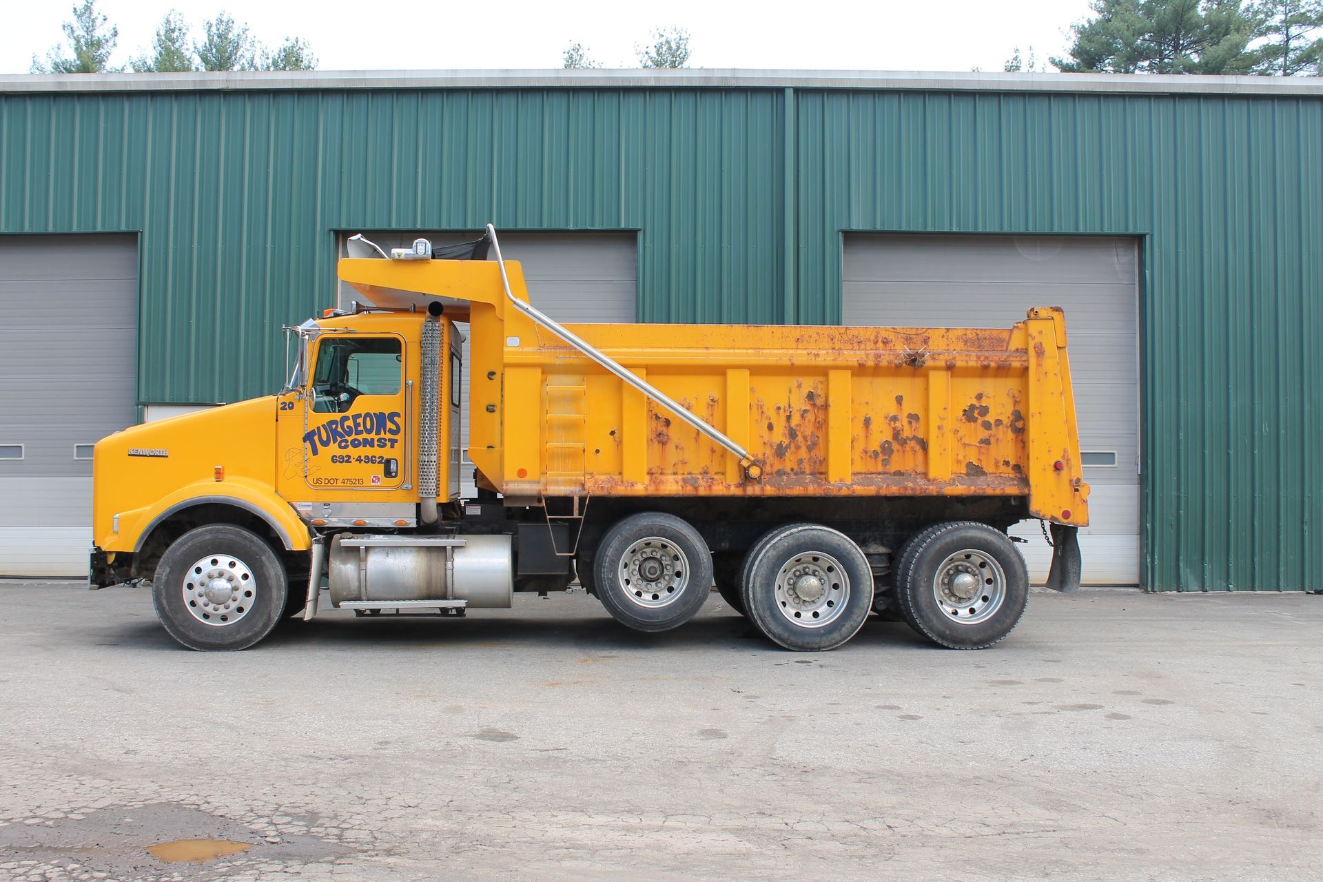 A yellow dump truck is parked in front of a green building.