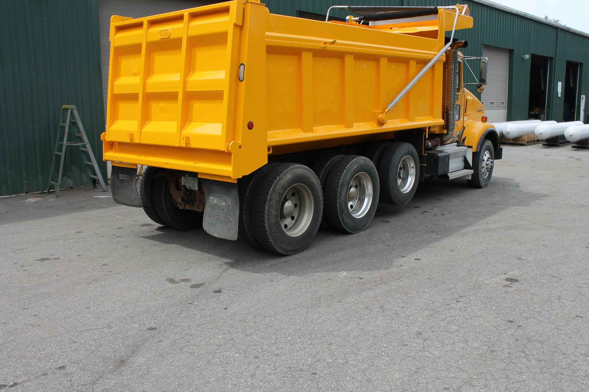 A yellow dump truck is parked in front of a green building