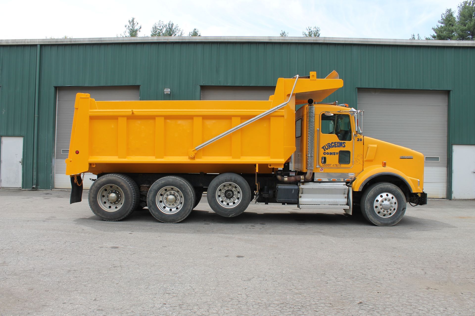 A yellow dump truck is parked in front of a green building.
