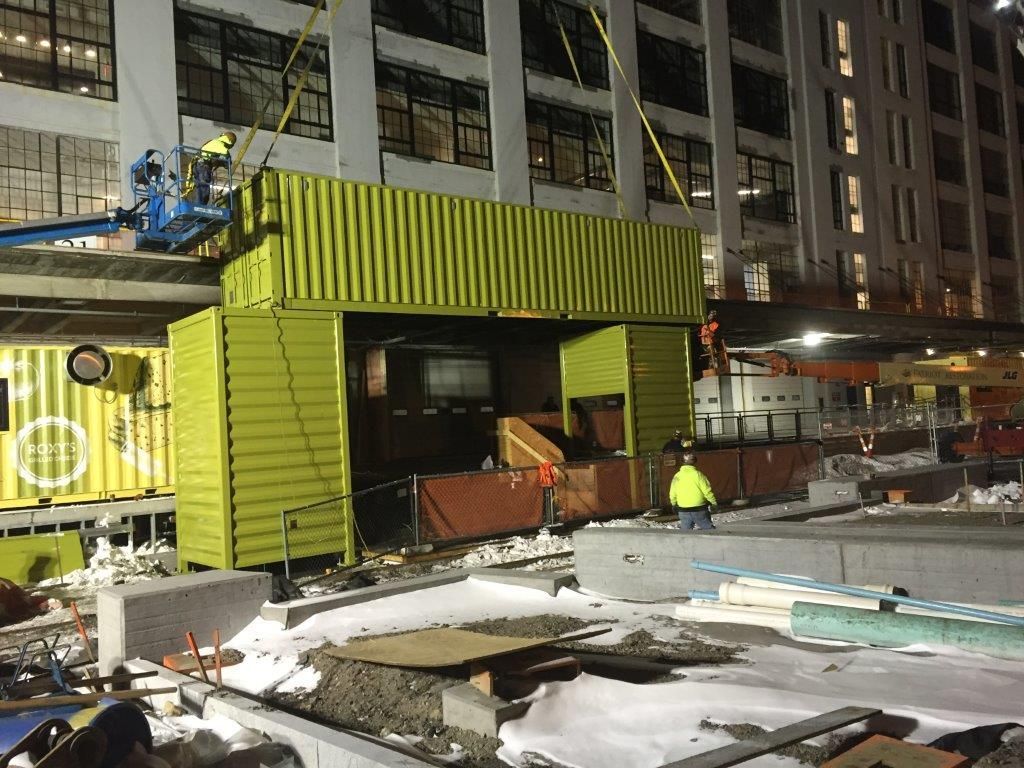 A construction site with a yellow container being lifted by a crane.