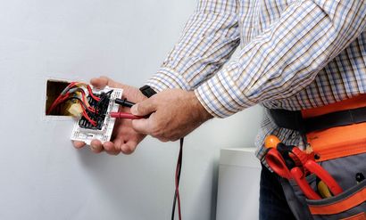 An electrician is working on an electrical outlet on a wall.
