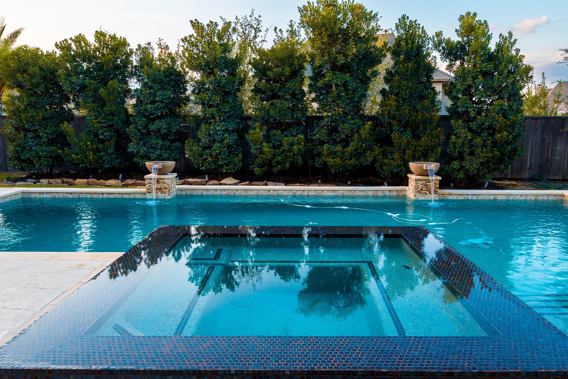 blue water, stone deck, green trees, two decorative urns, and a clear sky