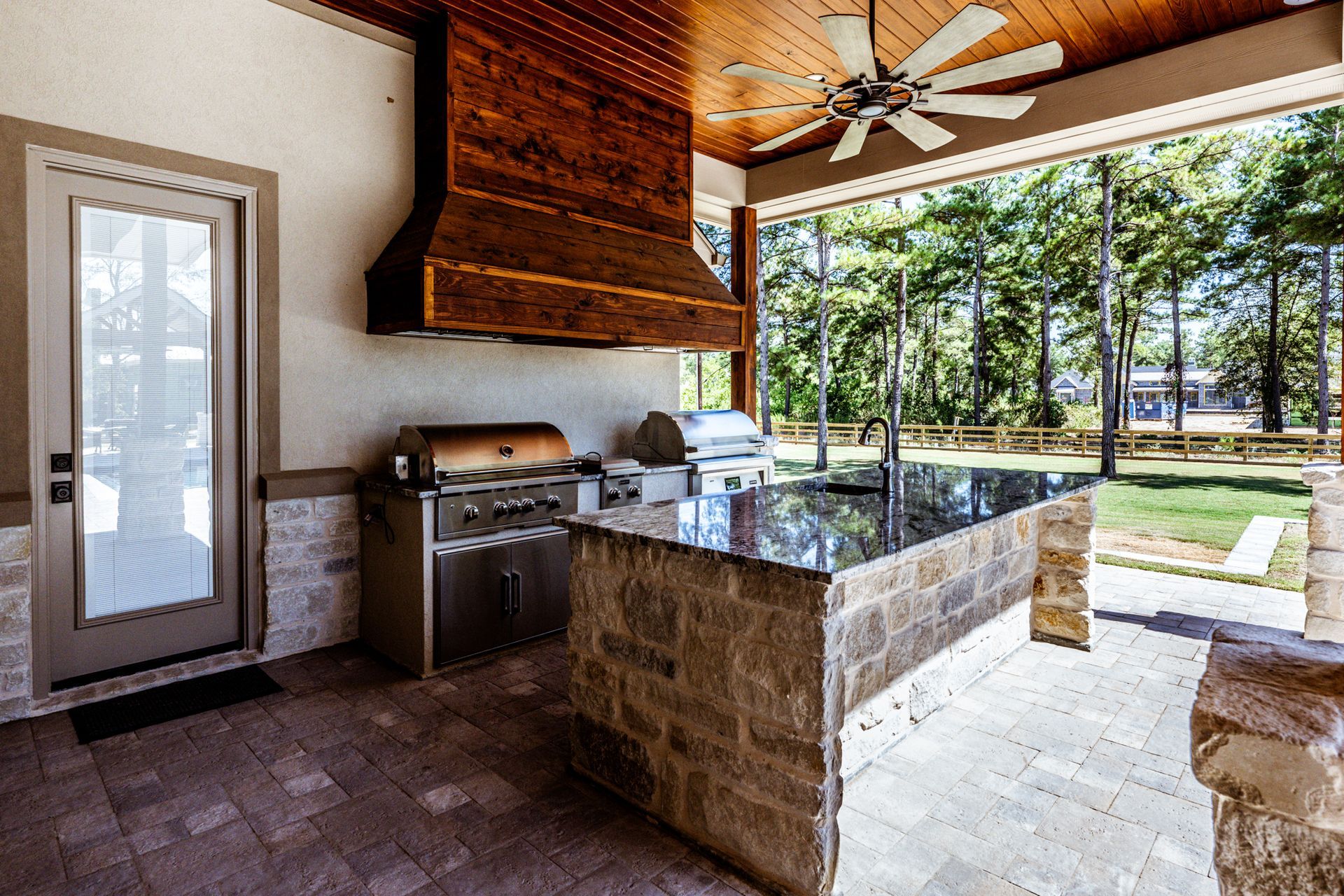 Outdoor kitchen with stainless steel grill, stone countertop, and wooden hood.