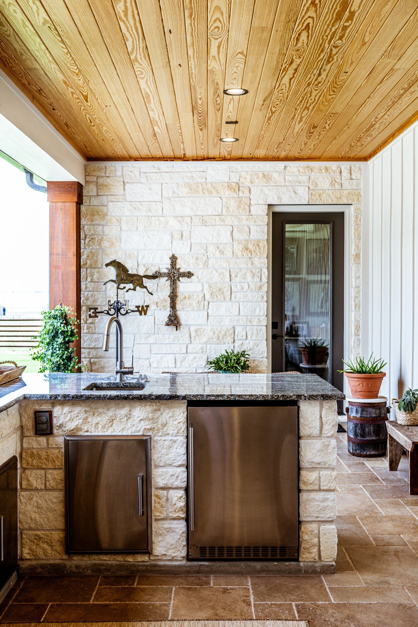 Outdoor kitchen with stone counters, stainless steel appliances, and wooden ceiling.