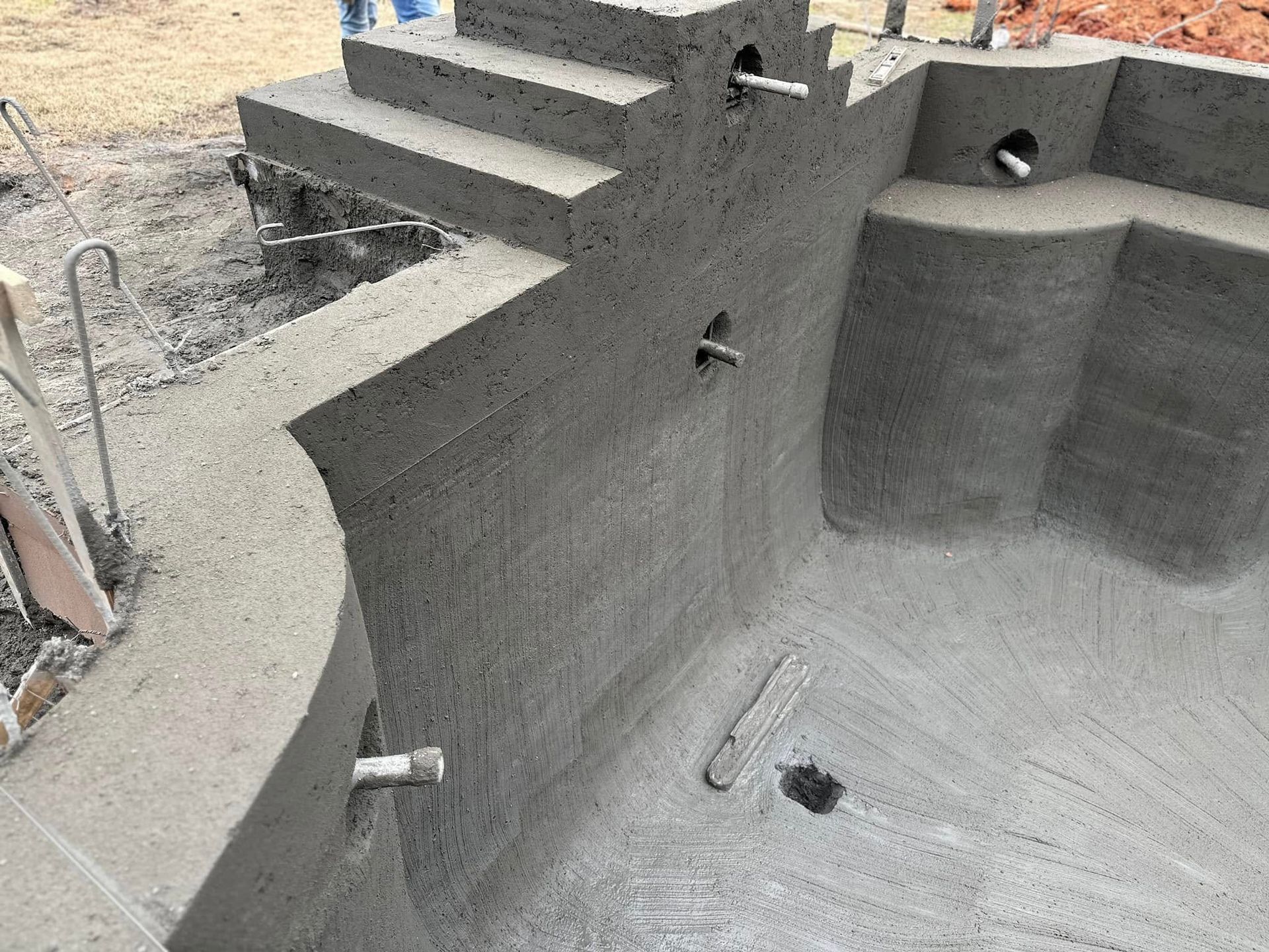 A swimming pool is being built with concrete and stairs.