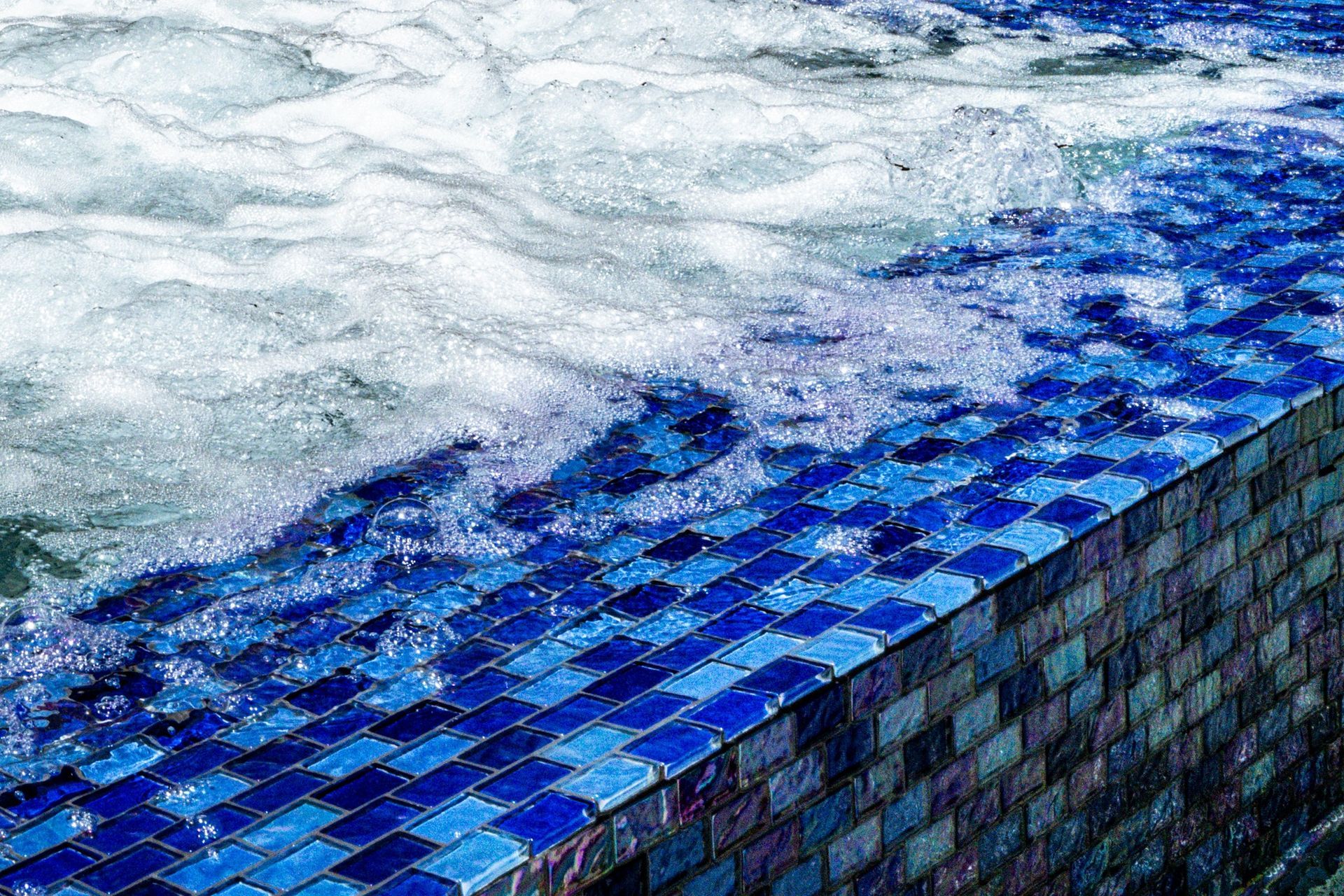 A swimming pool with blue tiles and bubbles coming out of it.
