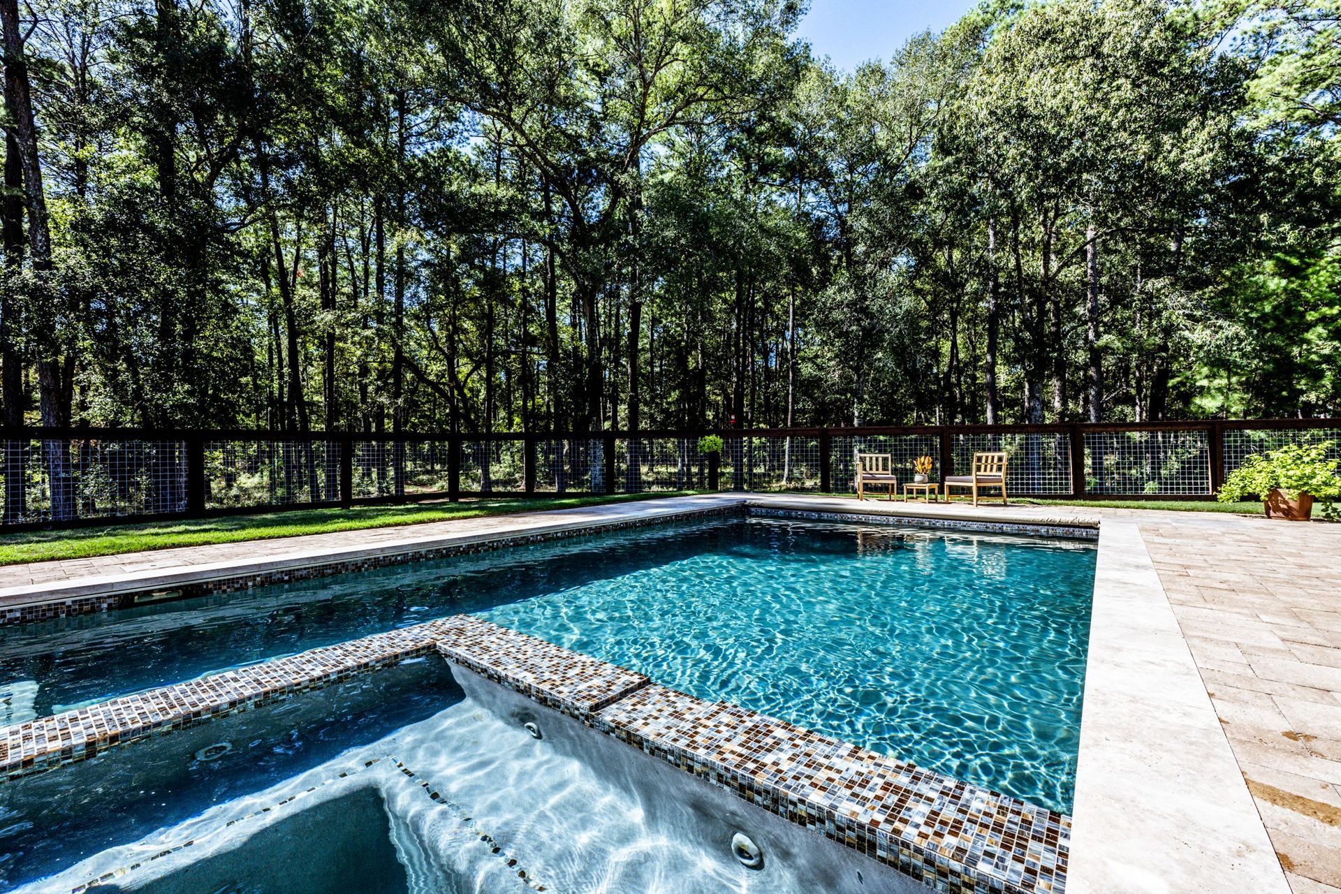A large swimming pool with a hot tub in the backyard surrounded by trees.