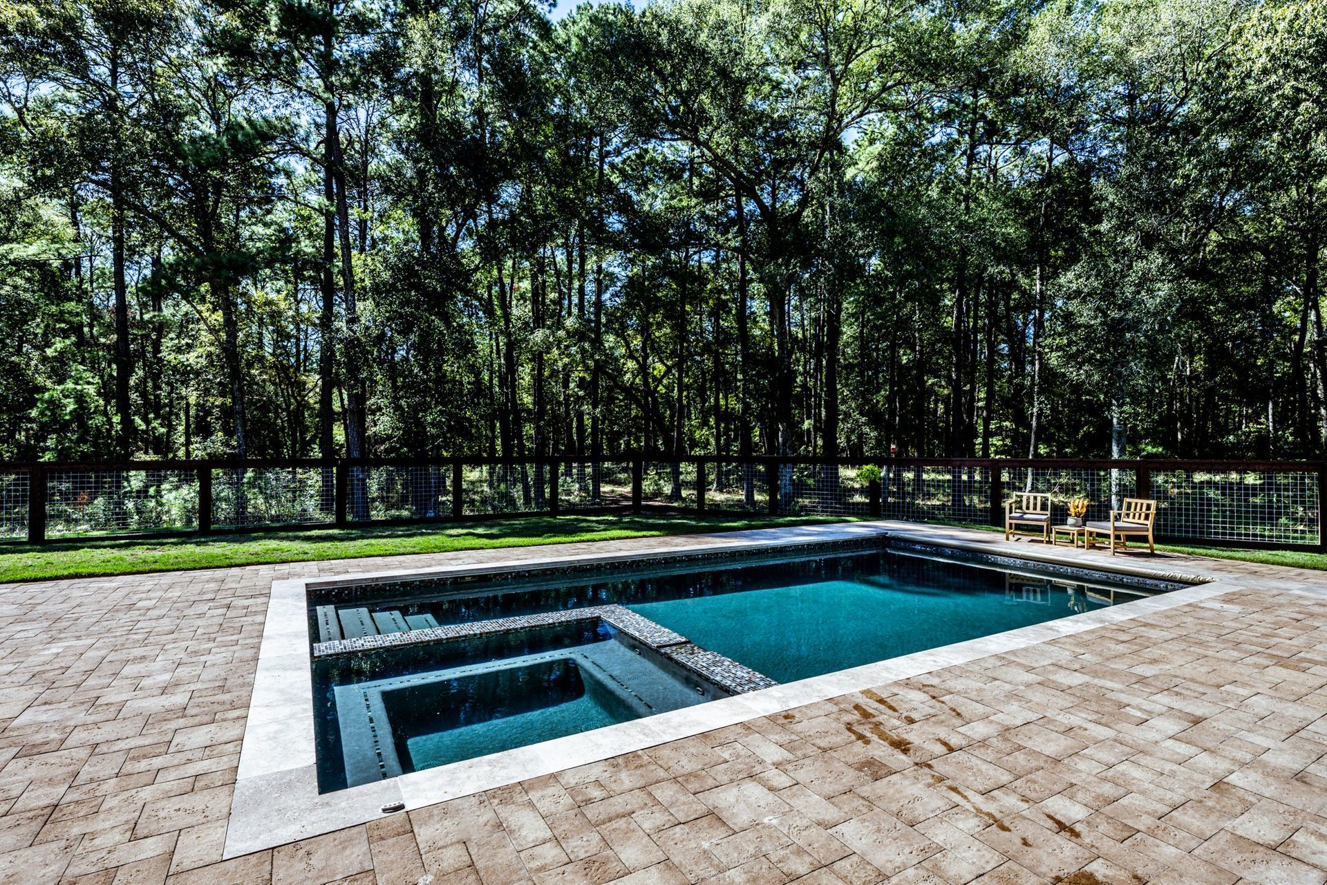 A large swimming pool is surrounded by trees and a brick patio.