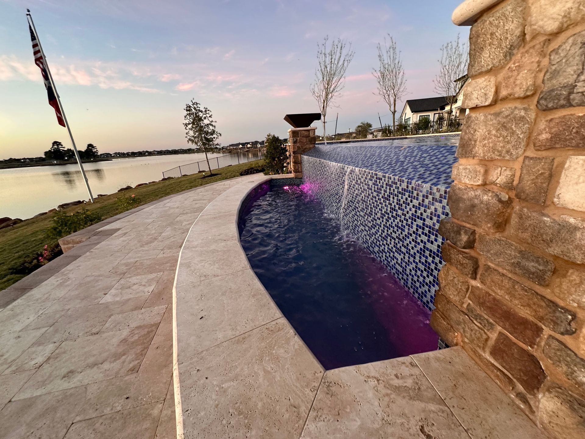 A large swimming pool is surrounded by a stone wall and a large body of water.