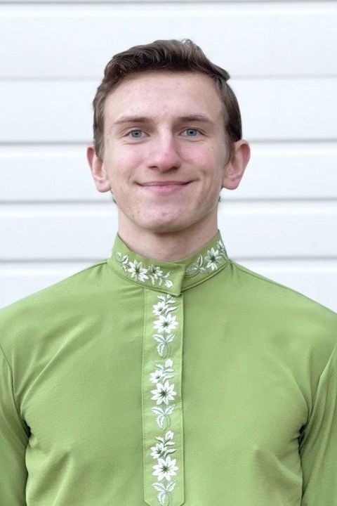 A young man wearing a green shirt and tie is smiling.