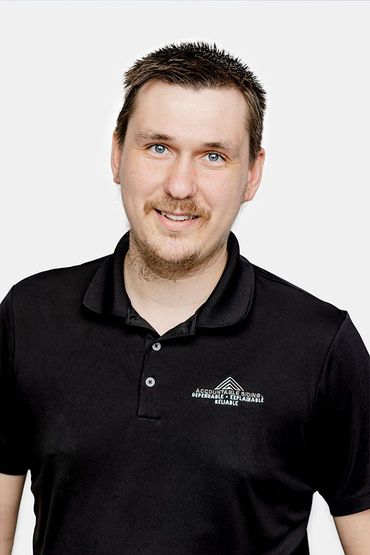 A man with a beard is wearing a black polo shirt and smiling.