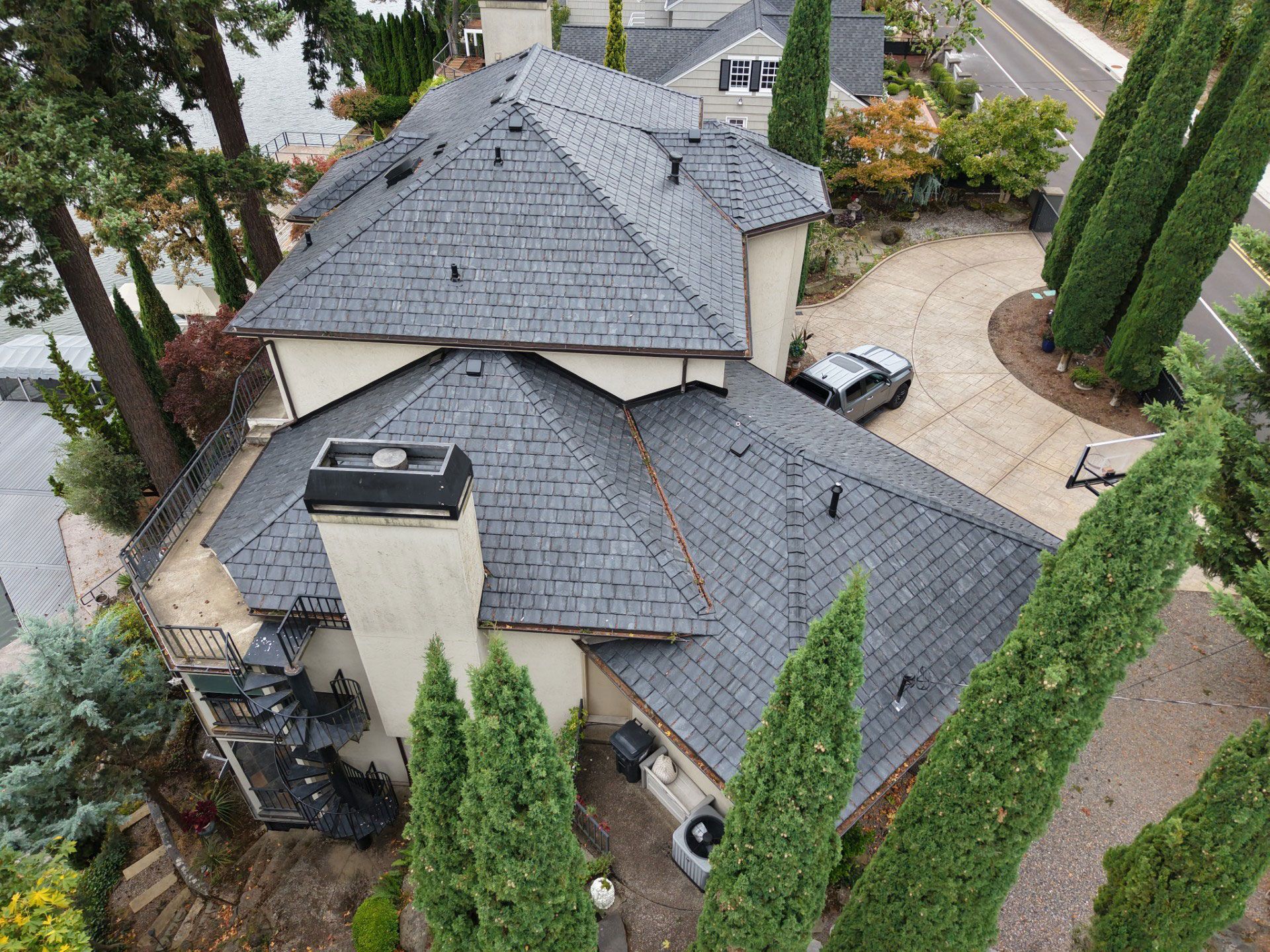 Aerial view of a large gray-roofed house surrounded by trees and a curved driveway.