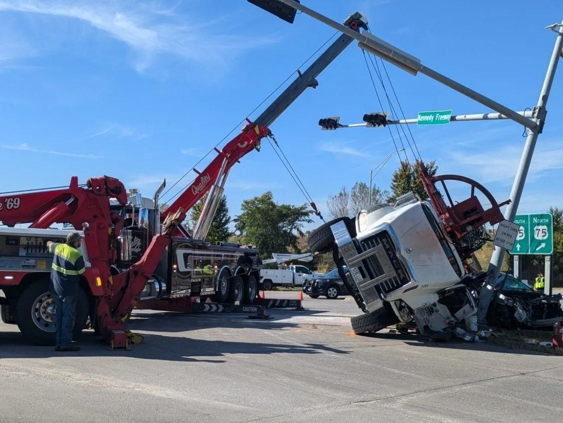 A tow truck lifting a semi-truck involved in a traffic accident near a street intersection.