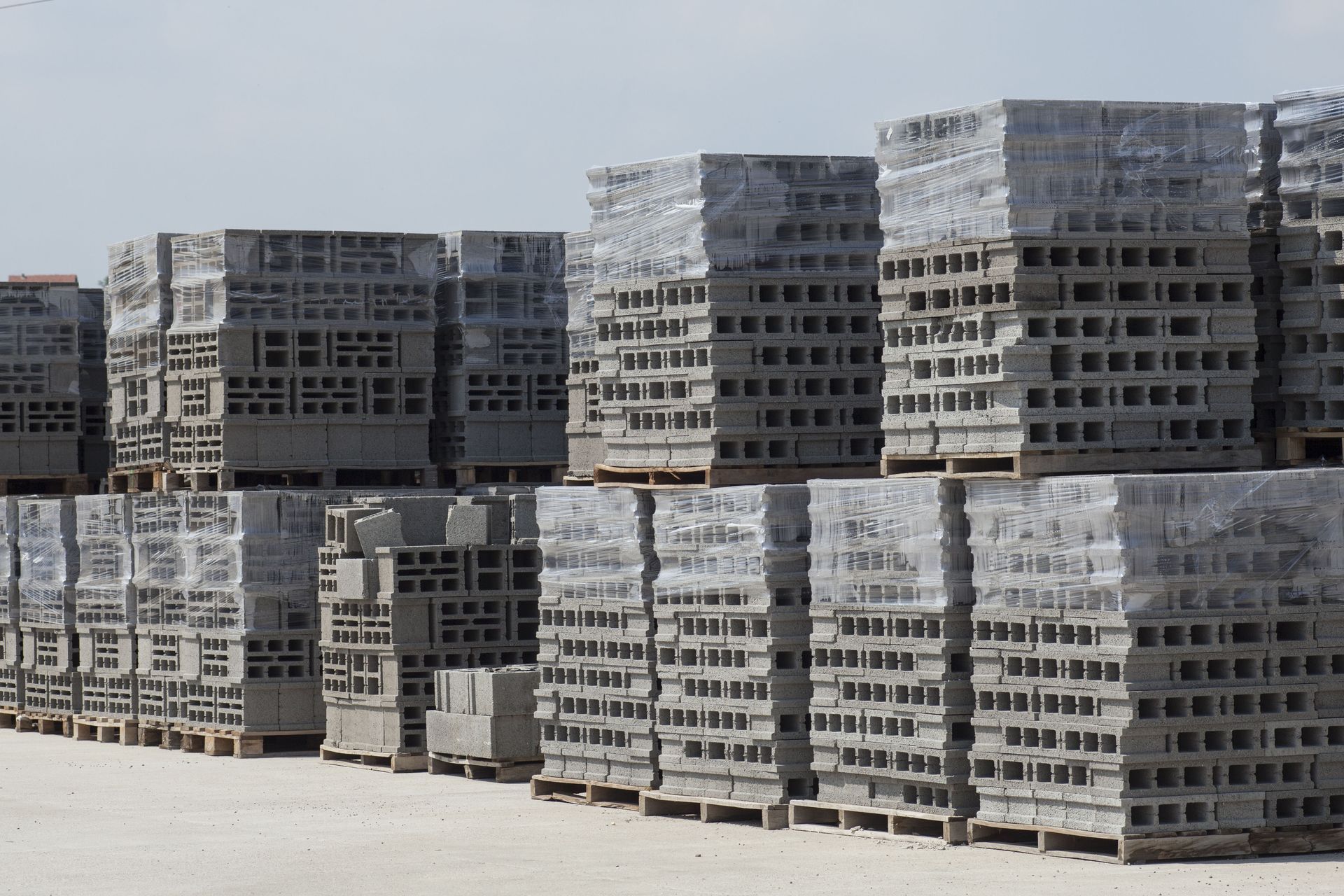 Stacks of gray concrete blocks wrapped in plastic on wooden pallets.