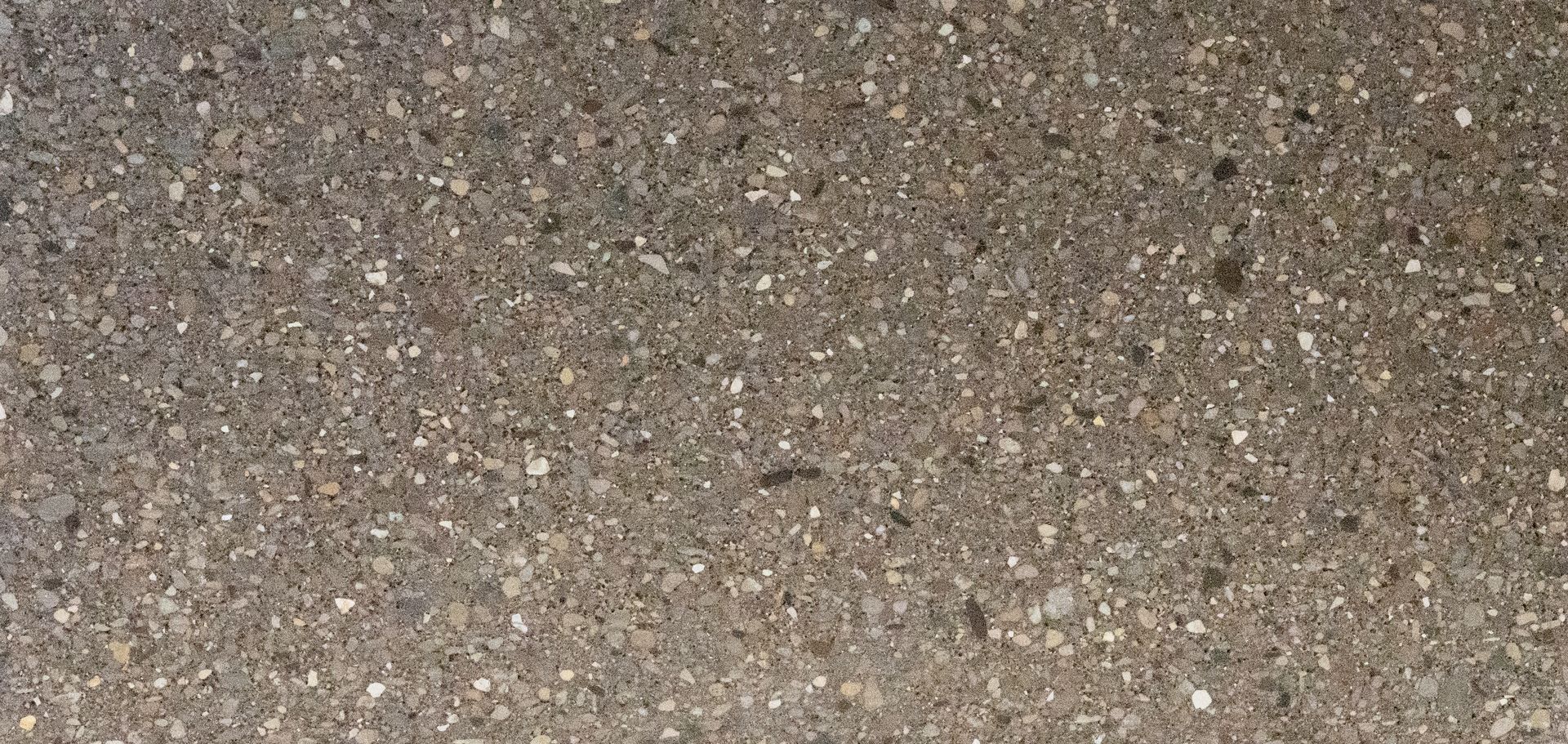 Close-up of rough gray-brown gravel or asphalt surface with small pebbles.