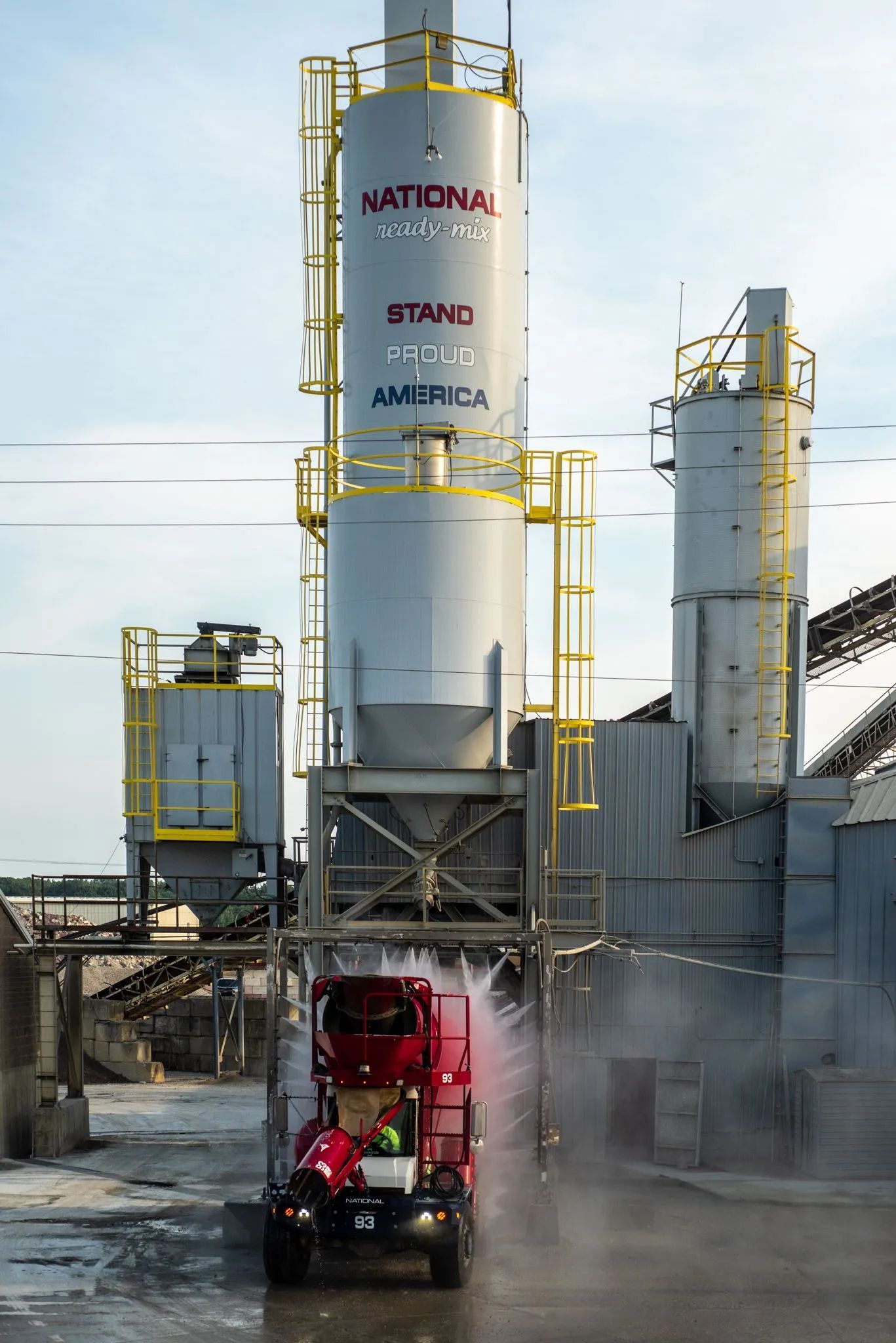 Red truck loading under industrial silos, spraying water.