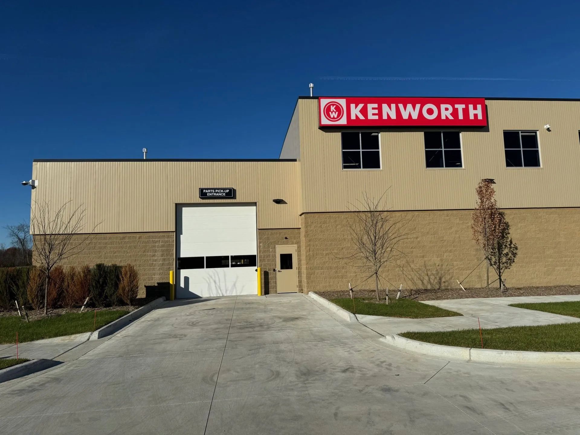 Kenworth service building with large garage door, red sign, and driveway.