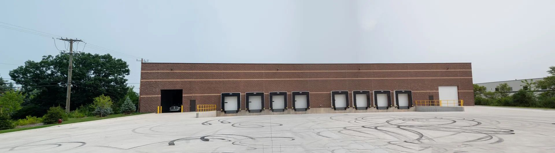 Warehouse exterior with multiple loading docks and a light-colored parking area under a cloudy sky.