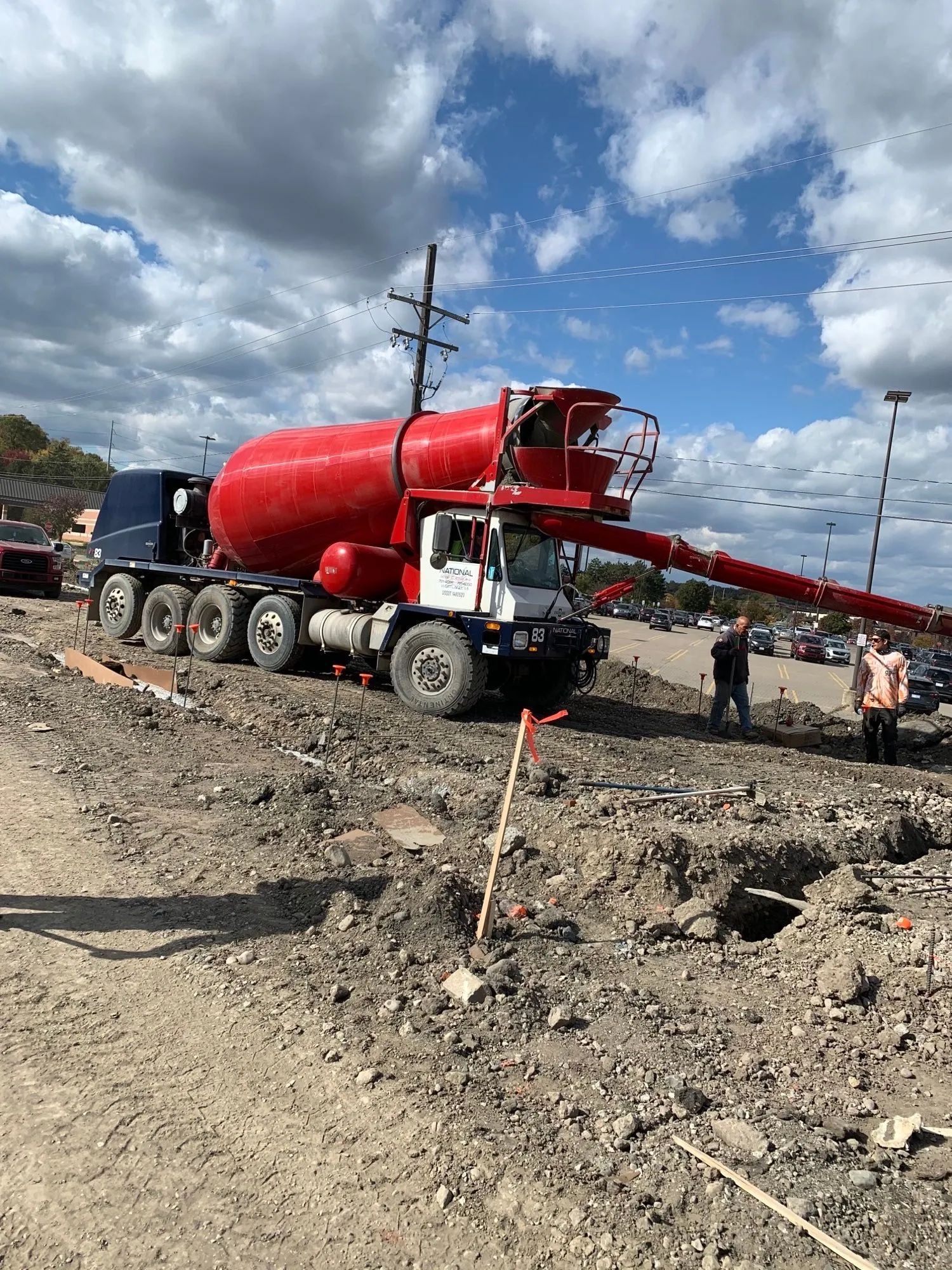 Red cement truck pouring concrete at a construction site on a sunny day.