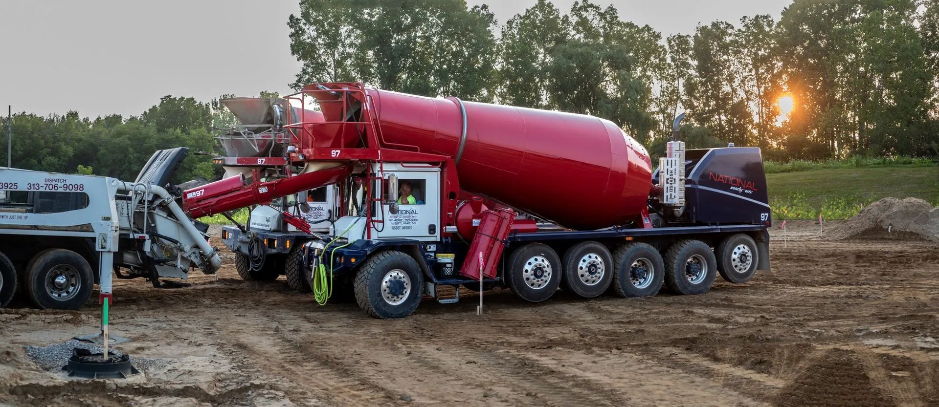 Concrete mixer trucks on a construction site at sunset.