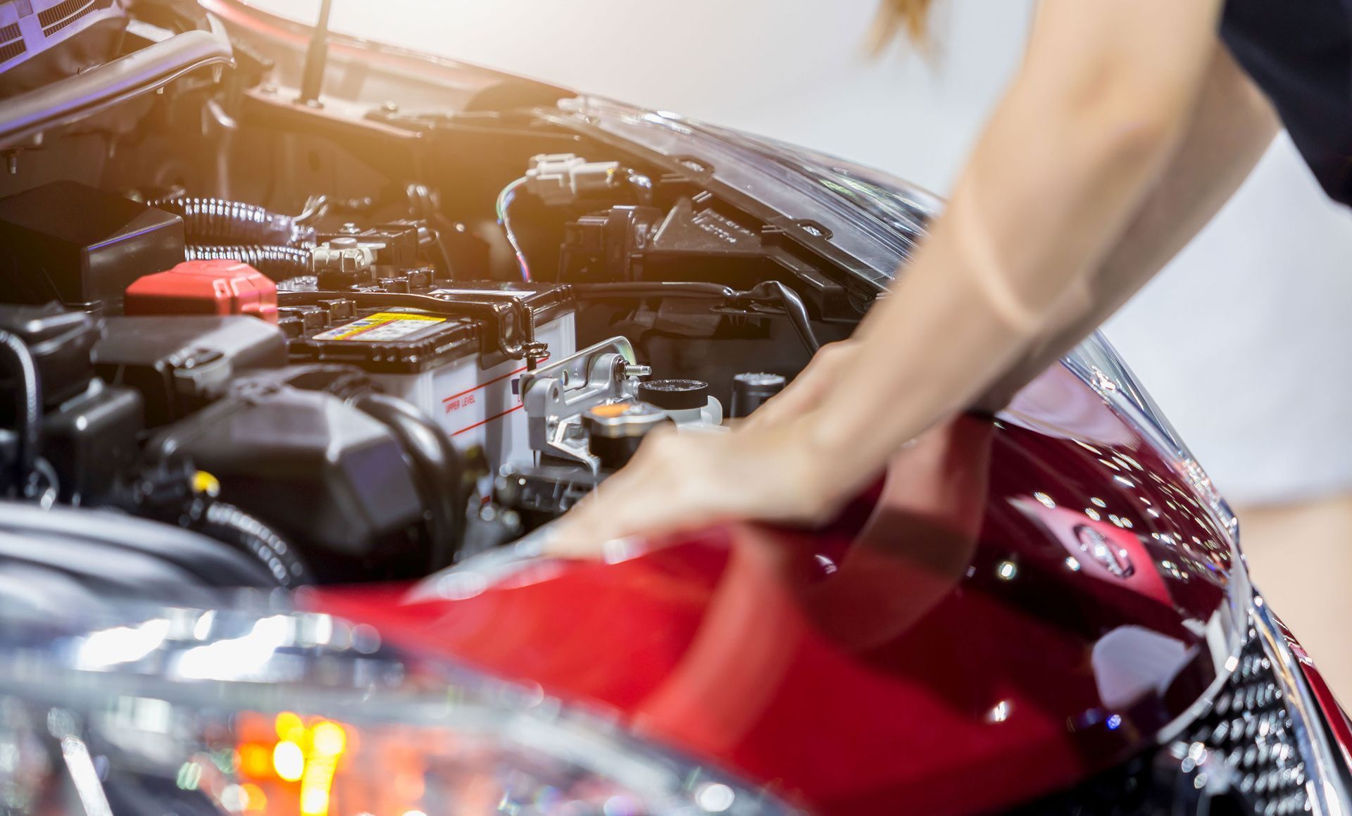 Person wiping down a red car engine bay.