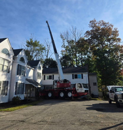Crane truck lifting equipment beside a white house in a residential driveway