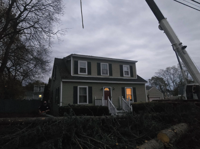 Dusk view of a two-story house with lit windows and a crane arm overhead behind bare trees.