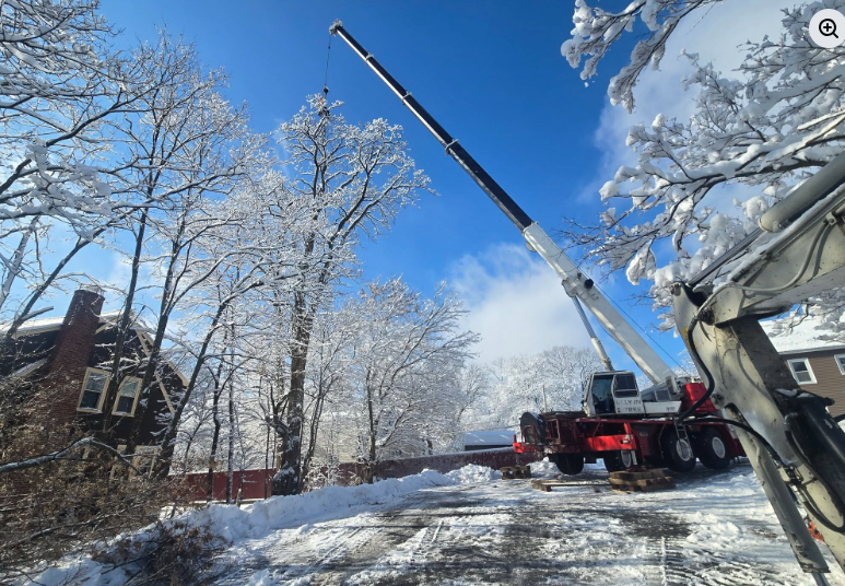 Crane truck lifting a worker basket beside a snowy house on a winter street