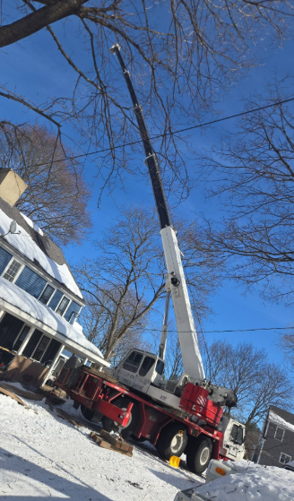 Crane truck lifting a utility pole near snowy houses under a clear blue sky