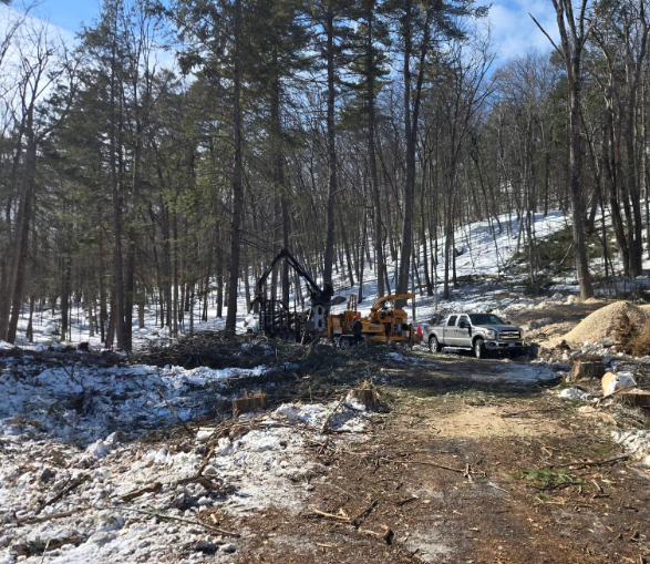 Construction equipment and a white truck on a snowy wooded hillside