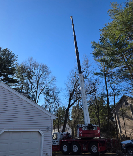 Crane lifting a long black beam beside a white garage under a blue sky