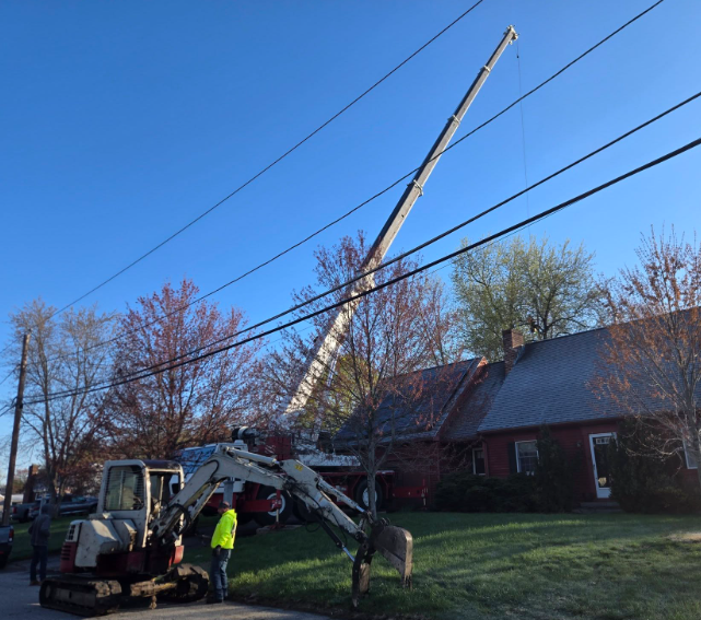 Construction crew lifting a fallen utility pole beside a house on a clear blue day