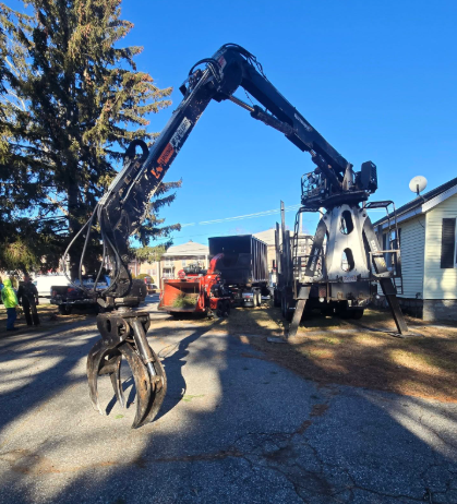 Long-armed excavator with grapple parked in a residential driveway under a blue sky