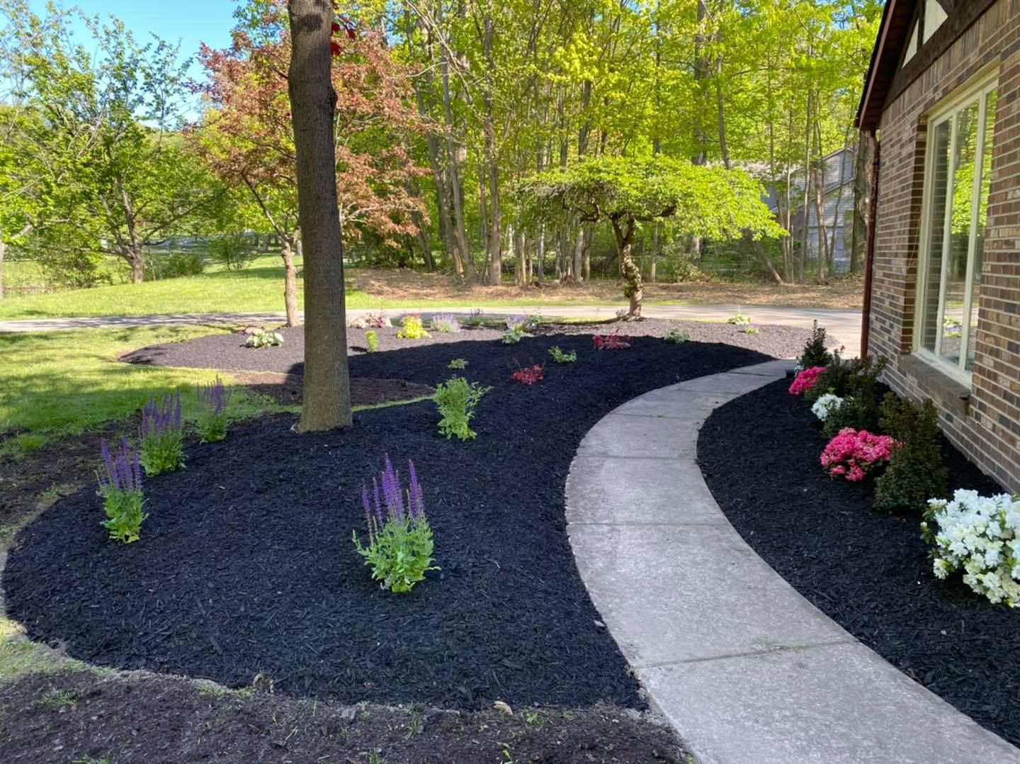 A walkway leading to a house surrounded by flowers and mulch.