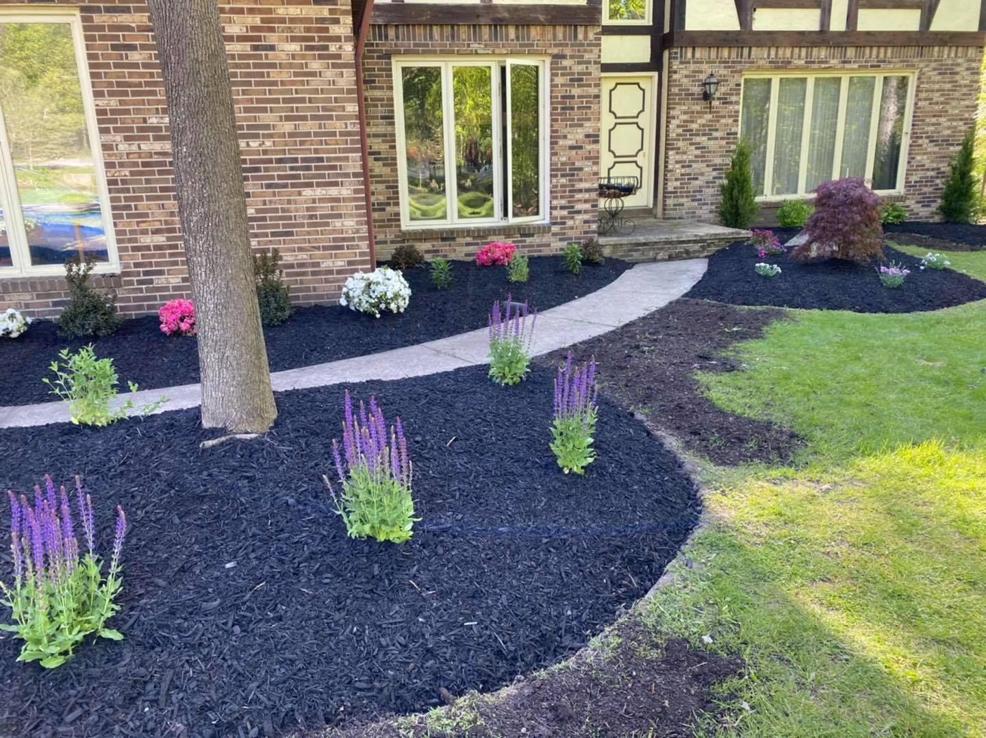A brick house with a lush green lawn and flowers in front of it.