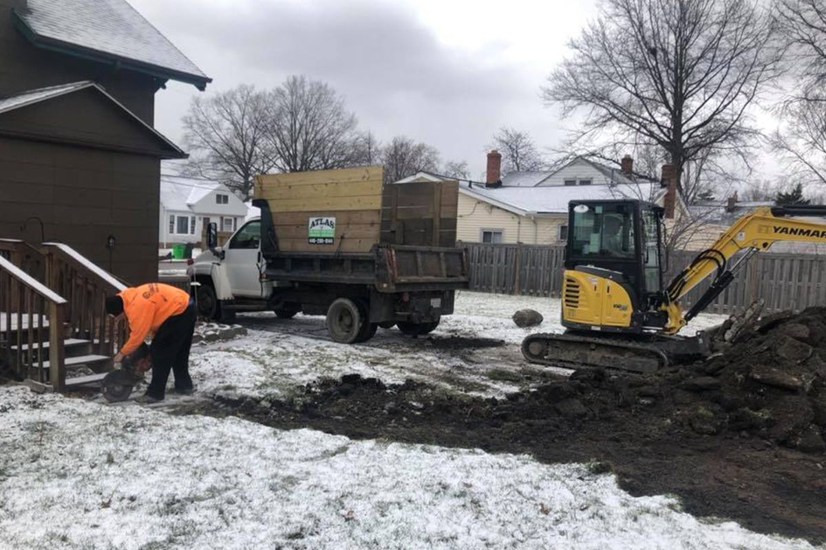 A man is digging in the snow in front of a dump truck.